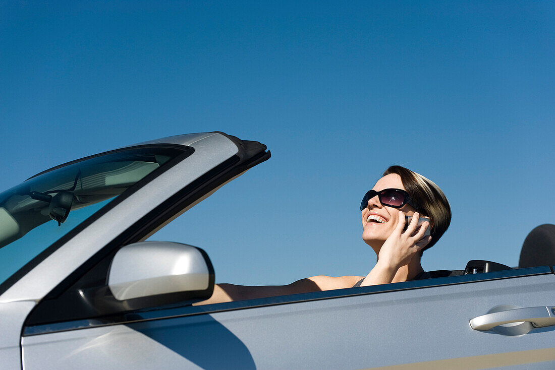 Woman talking on cell phone while driving convertible