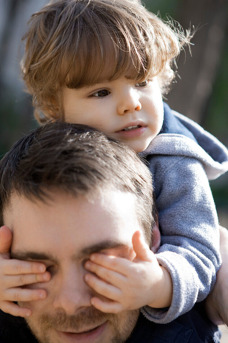 Toddler boy covering father's eyes with his hands, portrait