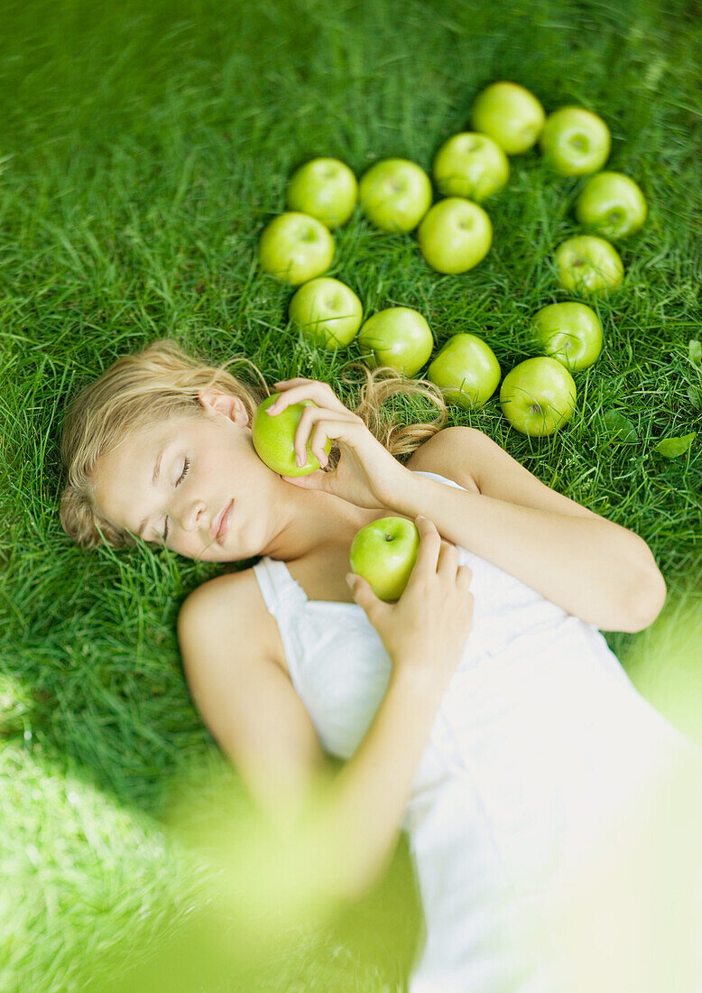 Frau im Gras liegend, neben herzförmig angeordneten Äpfeln