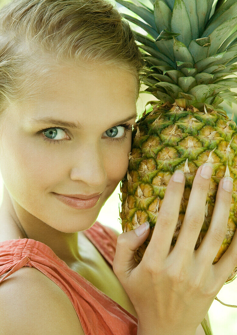 Woman holding pineapple next to face, smiling at camera