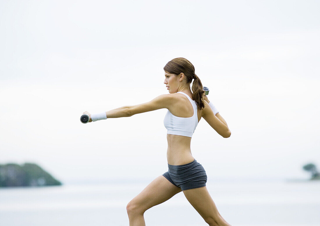 Junge Frau trainiert mit Gewichten, im Freien