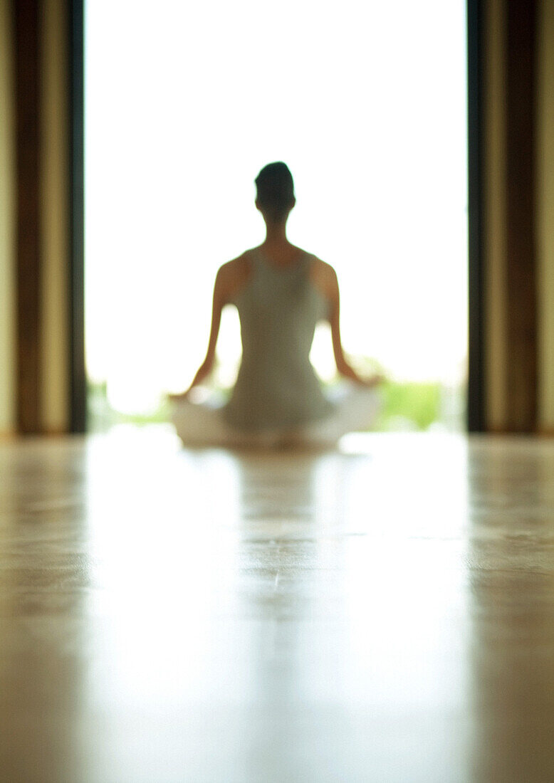 Yogaklasse, Frau im Lotussitz sitzend, unscharf und von hinten beleuchtet