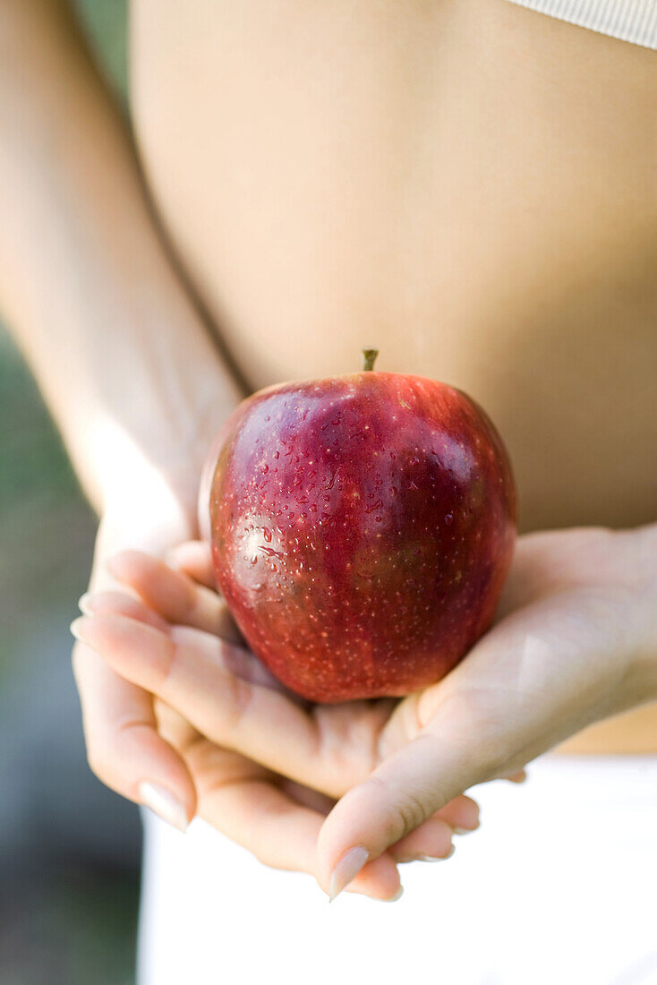 Woman holding apple in front of bare abdomen, close-up