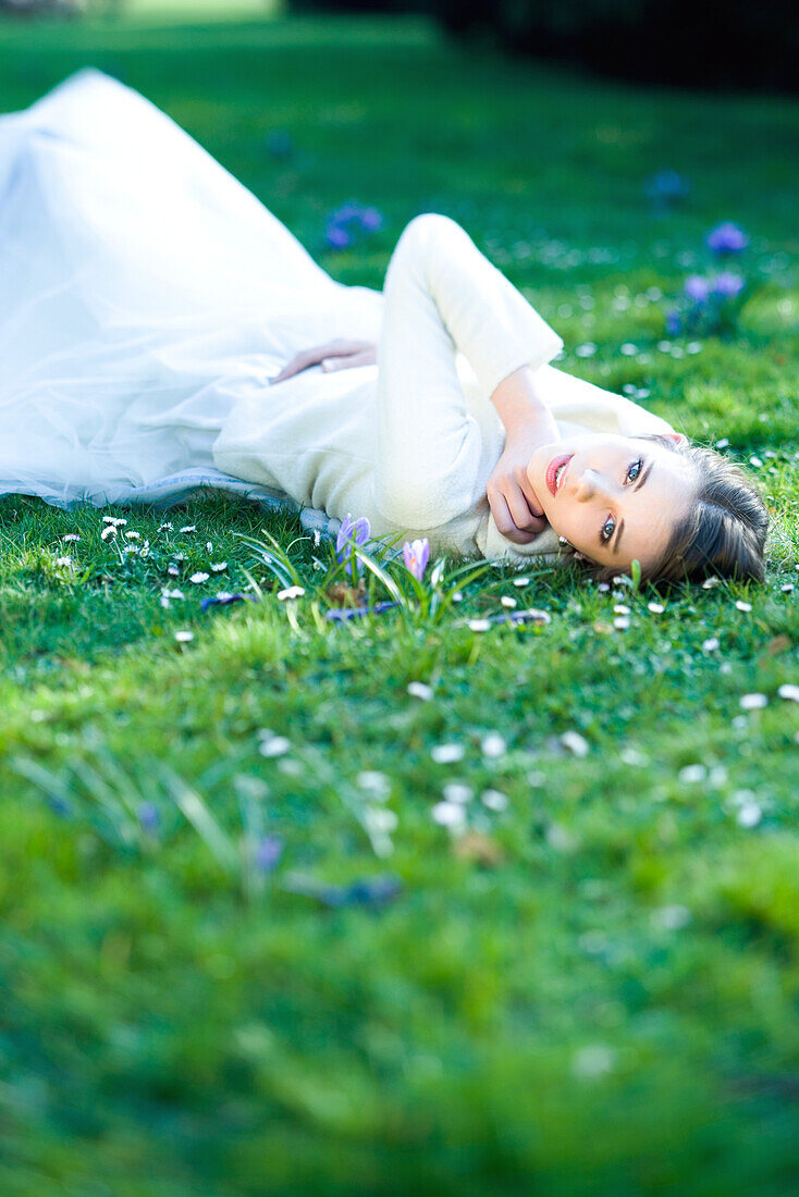 Teenage girl lying in grass, touching face, looking at camera