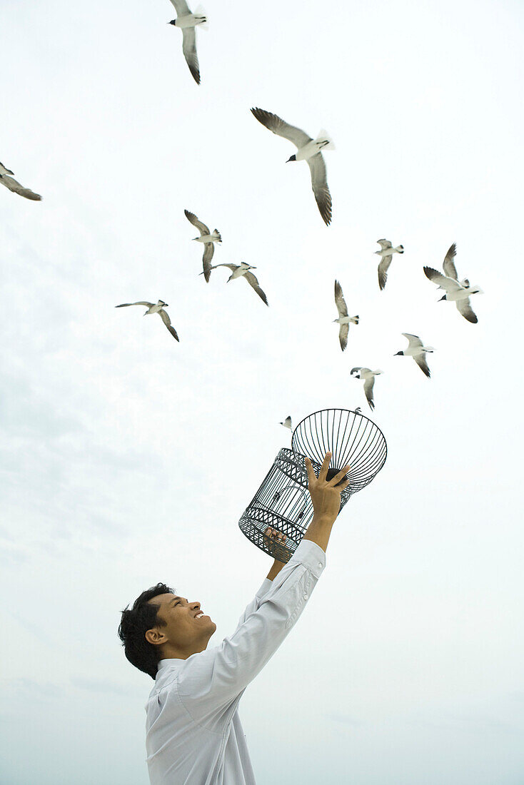 Man releasing bird outdoors, open cage in hand
