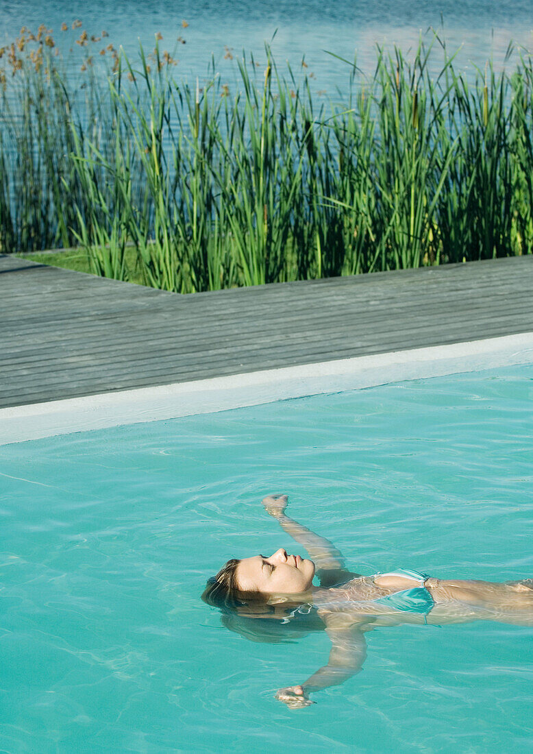 Woman floating on back in pool, waist up