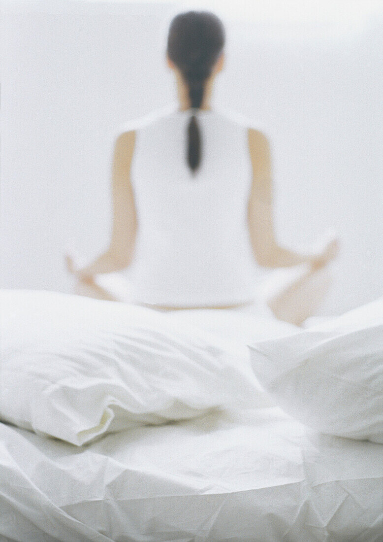 Frau sitzt im Lotussitz auf dem Bett, Rückansicht, unscharf