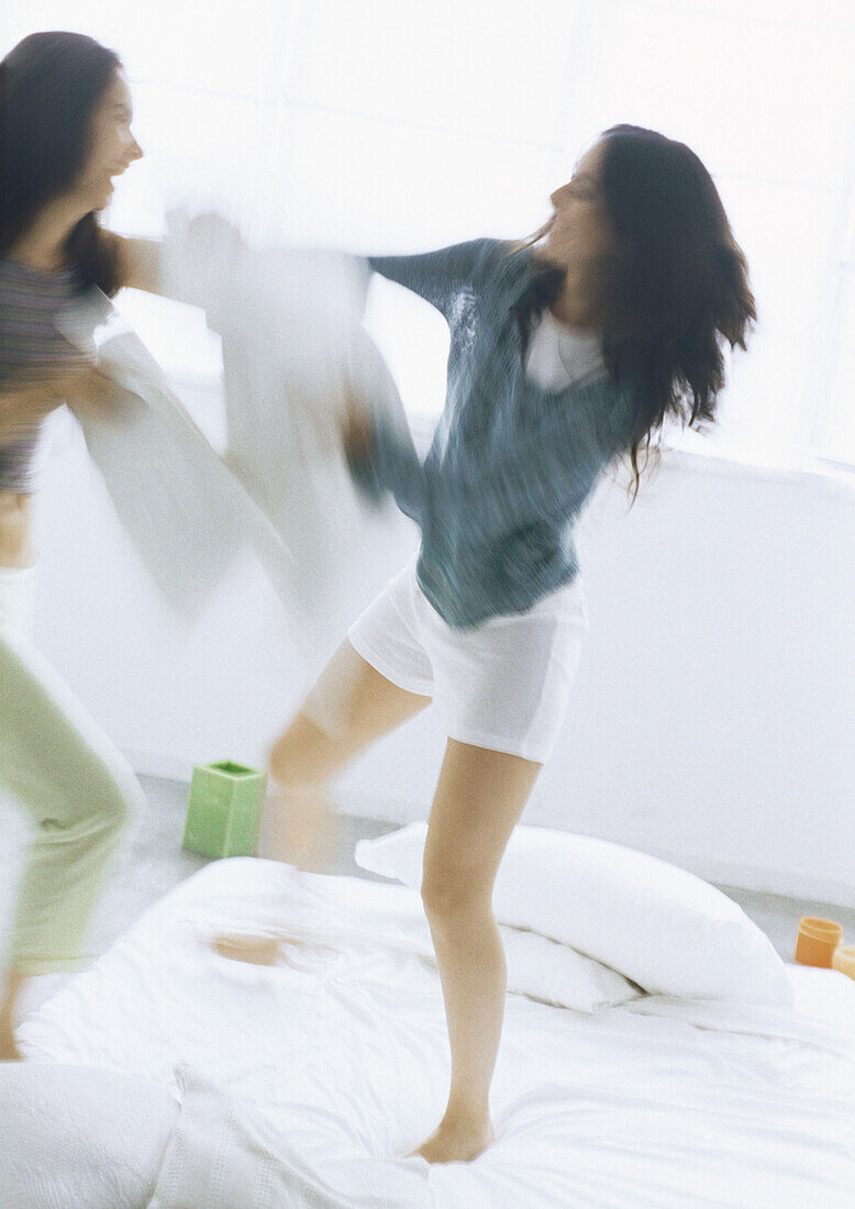 Two young women fighting with pillows, blurred motion