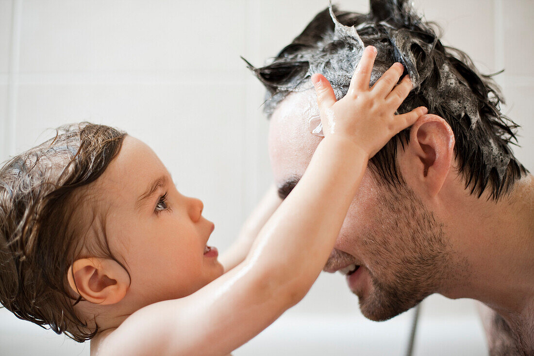 Toddler boy washing father's hair in bath