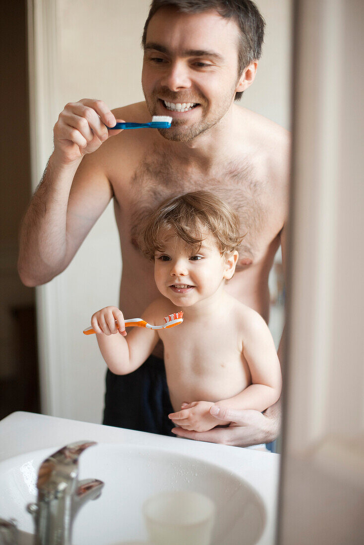 Father and toddler son brushing their teeth together