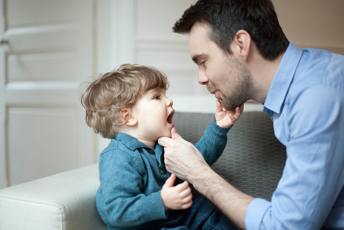 Father examining toddler son's teeth, portrait