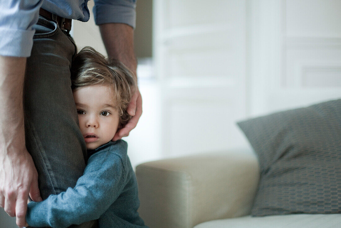 Toddler boy holding on to father's legs