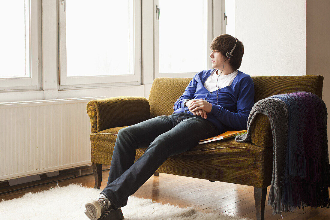 A teenage boy wearing headphones sitting on a couch