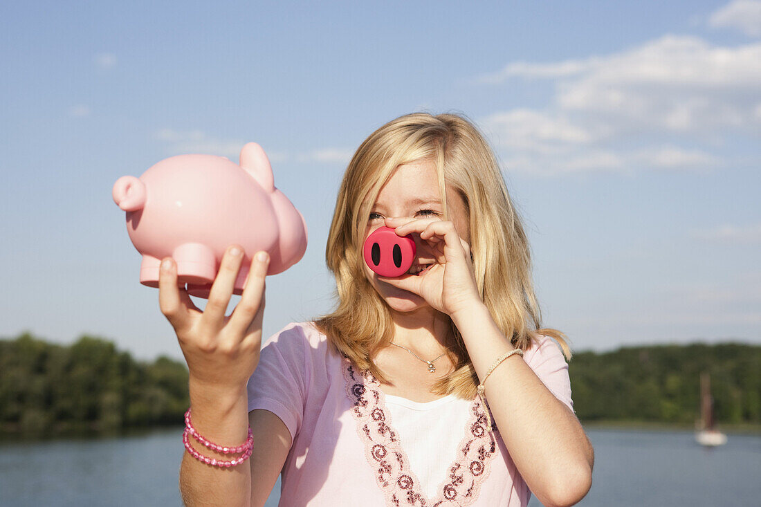 A teenage girl holding a pig nose and a piggy bank