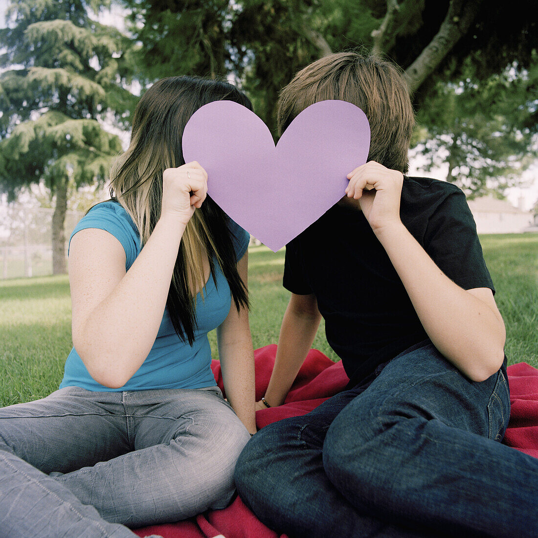 A teenage couple hiding behind a cut out heart
