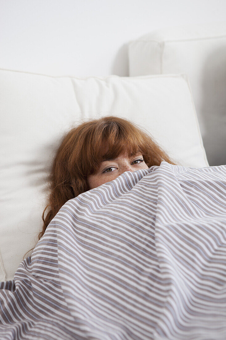 A woman peeking from behind a duvet in bed
