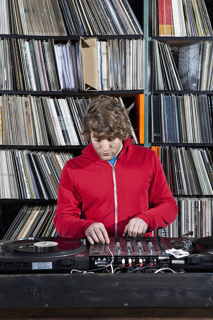 A young man using decks and a sound mixer at a record store