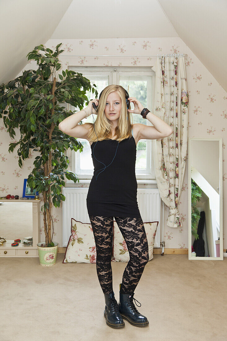 A punk teenage girl standing in a conservatively decorated bedroom