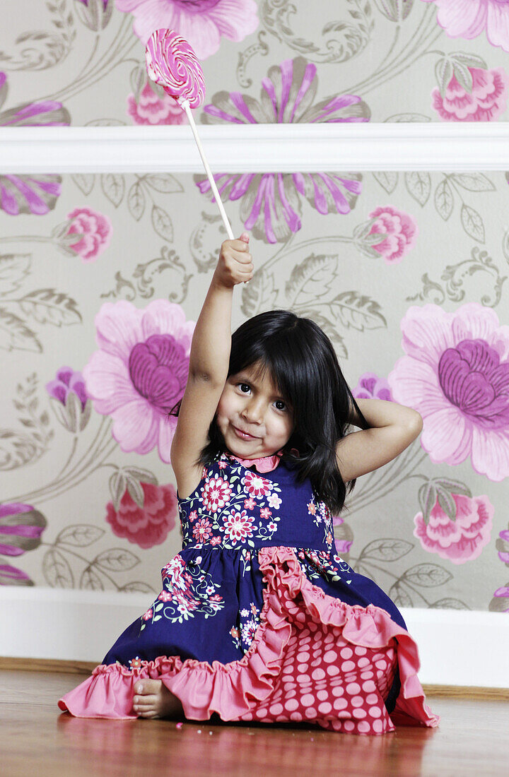 A young girl holding a swirl lollipop aloft
