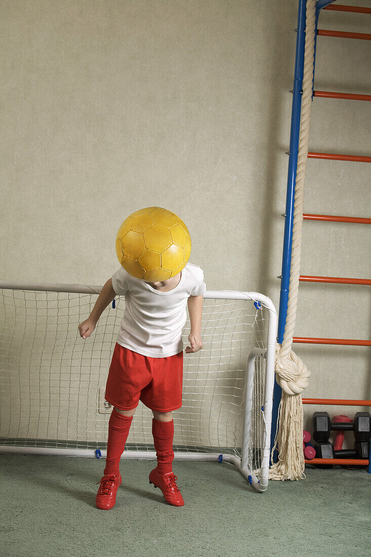 A young boy jumping to head butt a soccer ball away from a goal