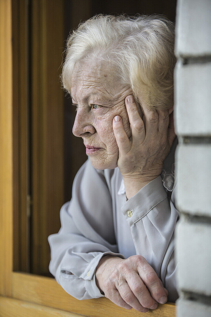 A senior woman leaning on a window sill, looking contemplative