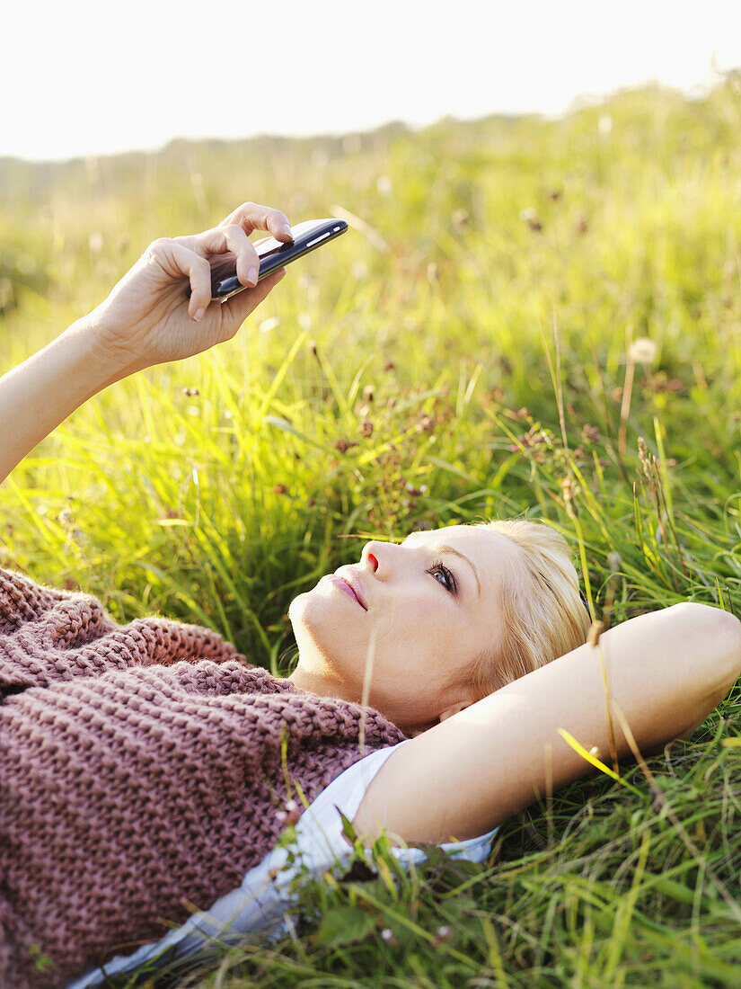 A woman lying in grass looking at her smart phone