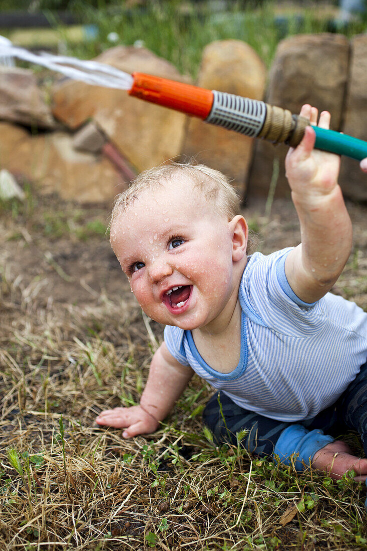 A laughing baby boy holding a garden hose