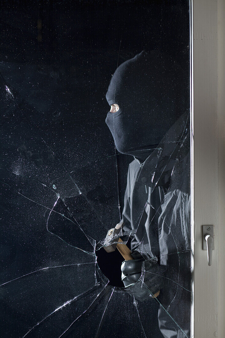 A criminal breaking into a window with a hammer