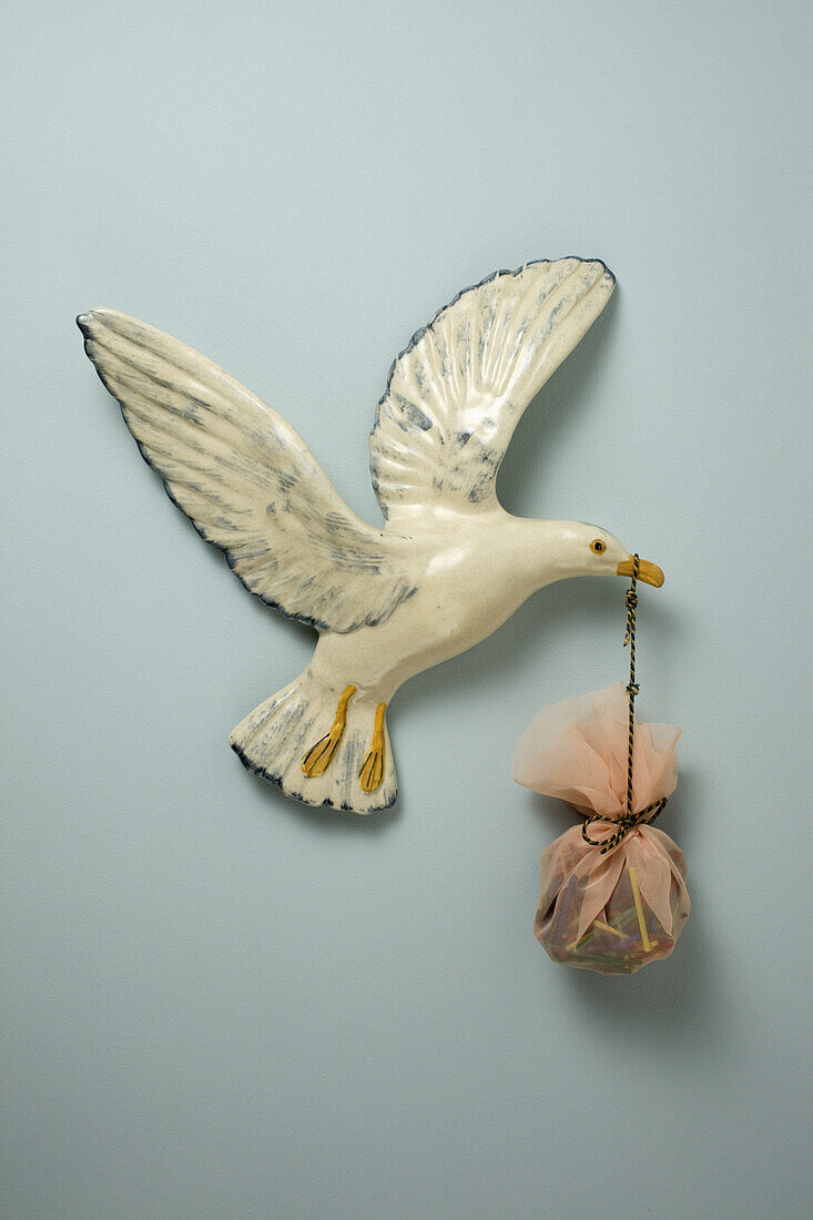 A plastic bird carrying a sack in its beak, hanging on wall