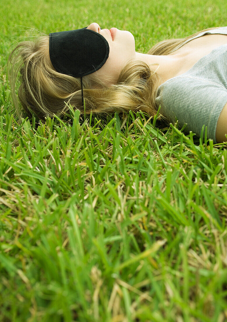 Young woman lying on grass, wearing eye mask