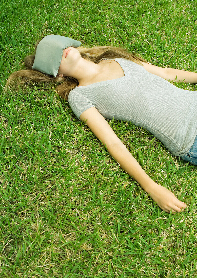 Young woman lying on grass with eye pillow covering eyes