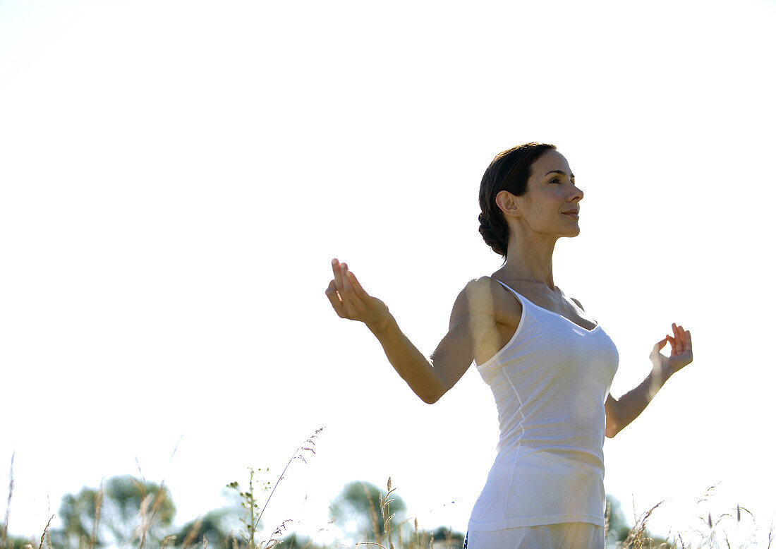 Woman standing outdoors with arms in yoga pose, low angle view
