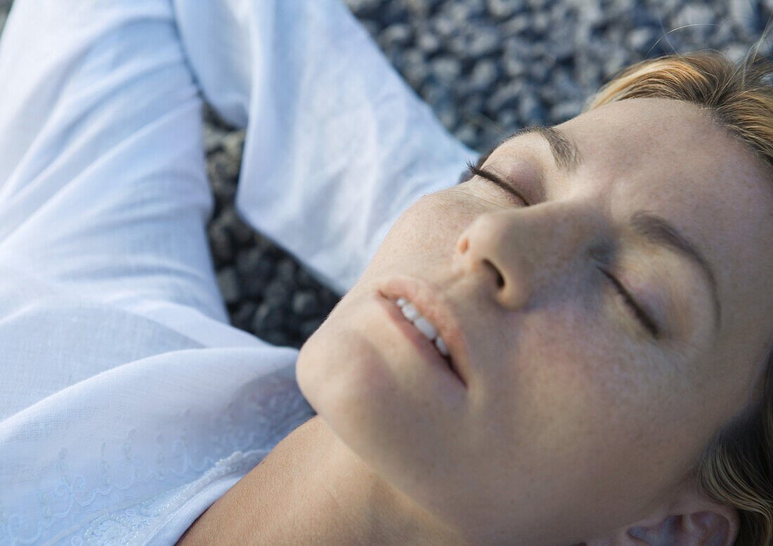 Woman lying on gravel with hands behind head, eyes closed, close-up