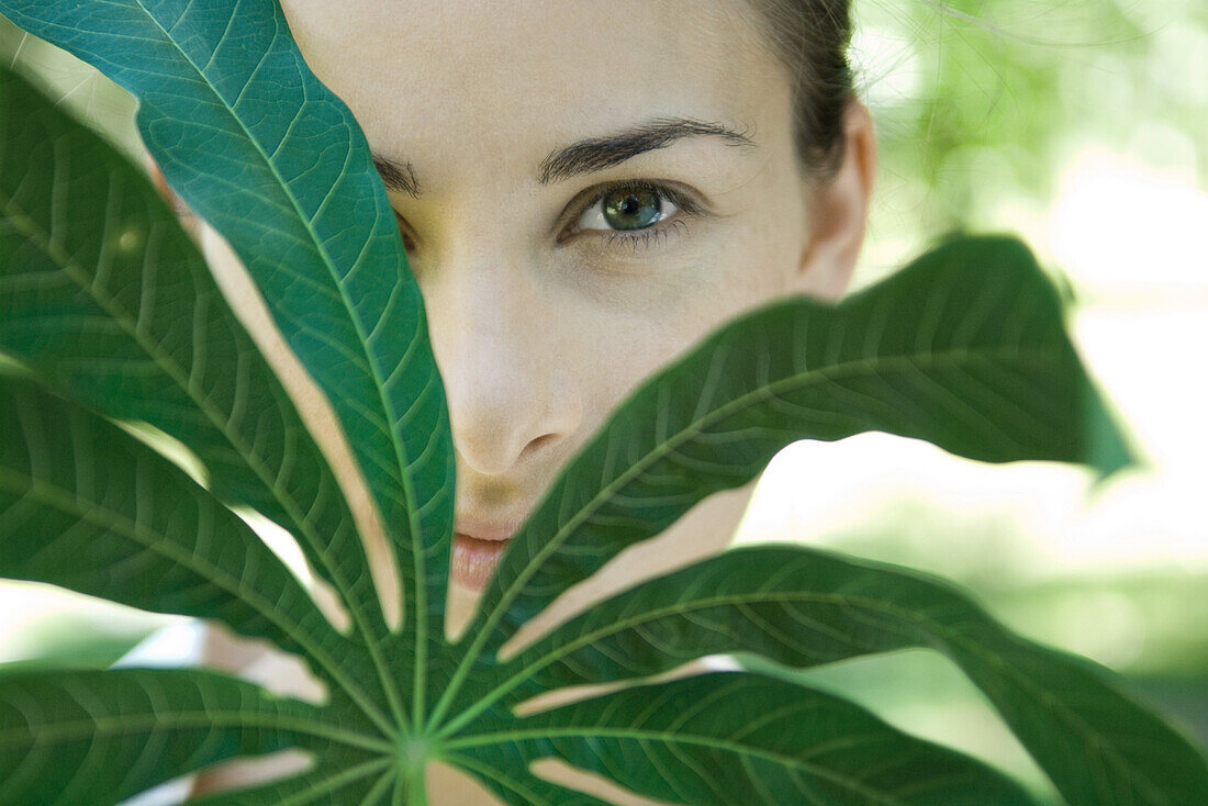 Frau blickt durch Blätter eines Maniokzweigs, Nahaufnahme