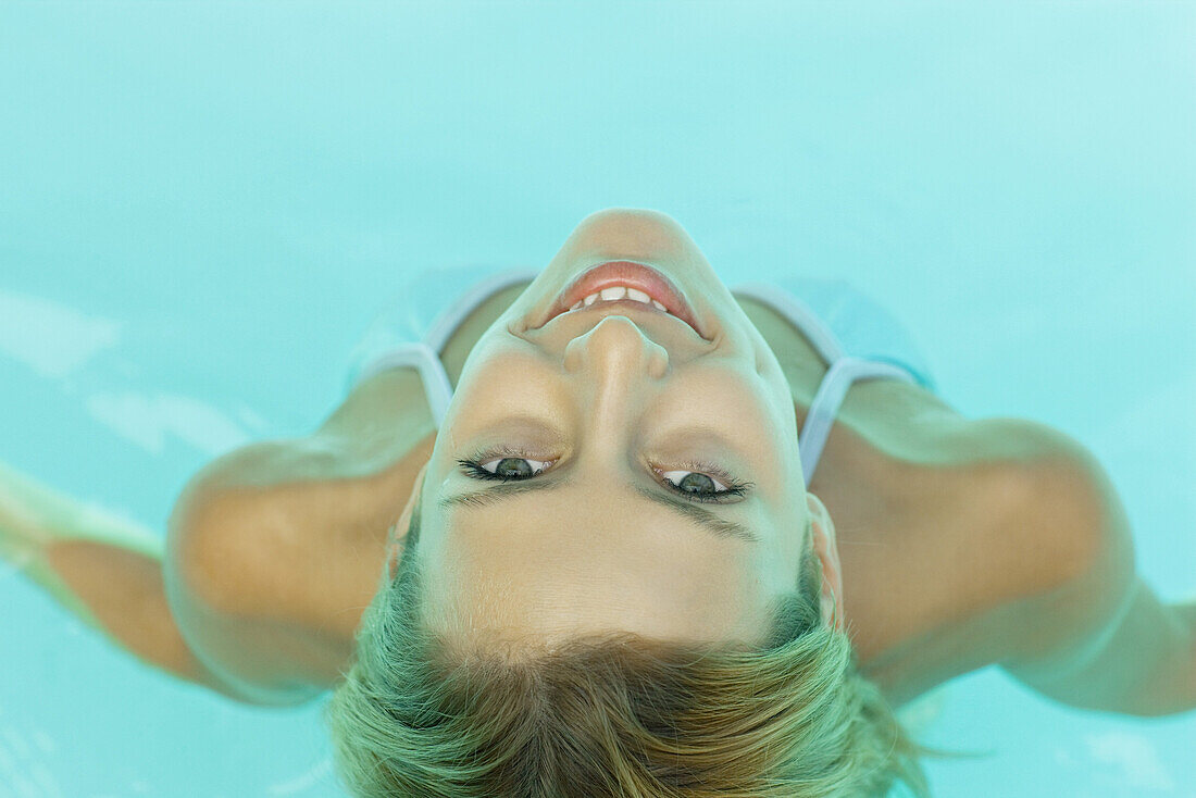 Young woman in pool, smiling at camera, view from directly above