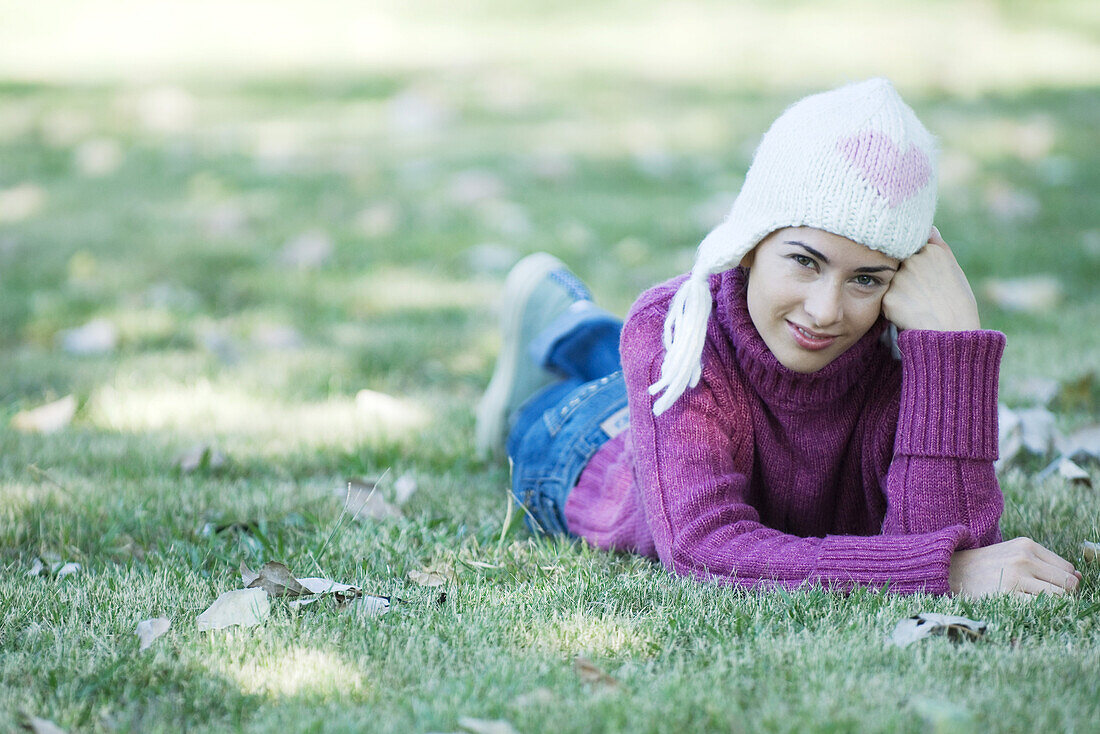 Young woman lying on grass, wearing knit hat and sweater
