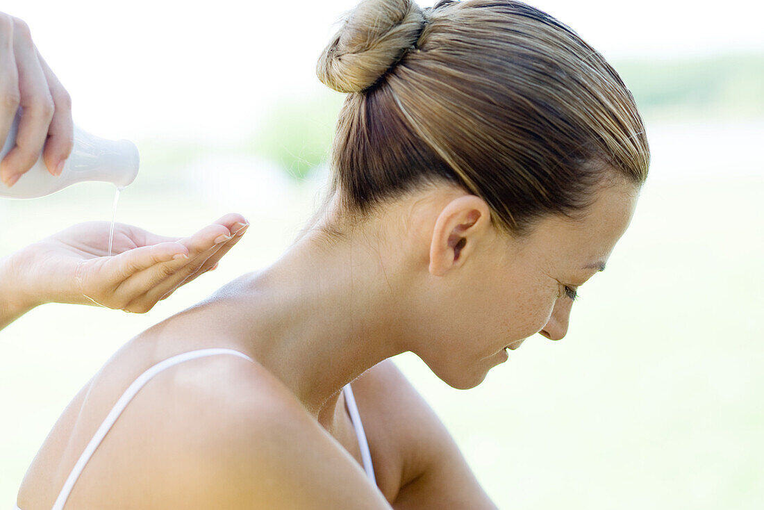Frau bei einer Rückenmassage, Massagetherapeutin gießt Öl in die Handfläche