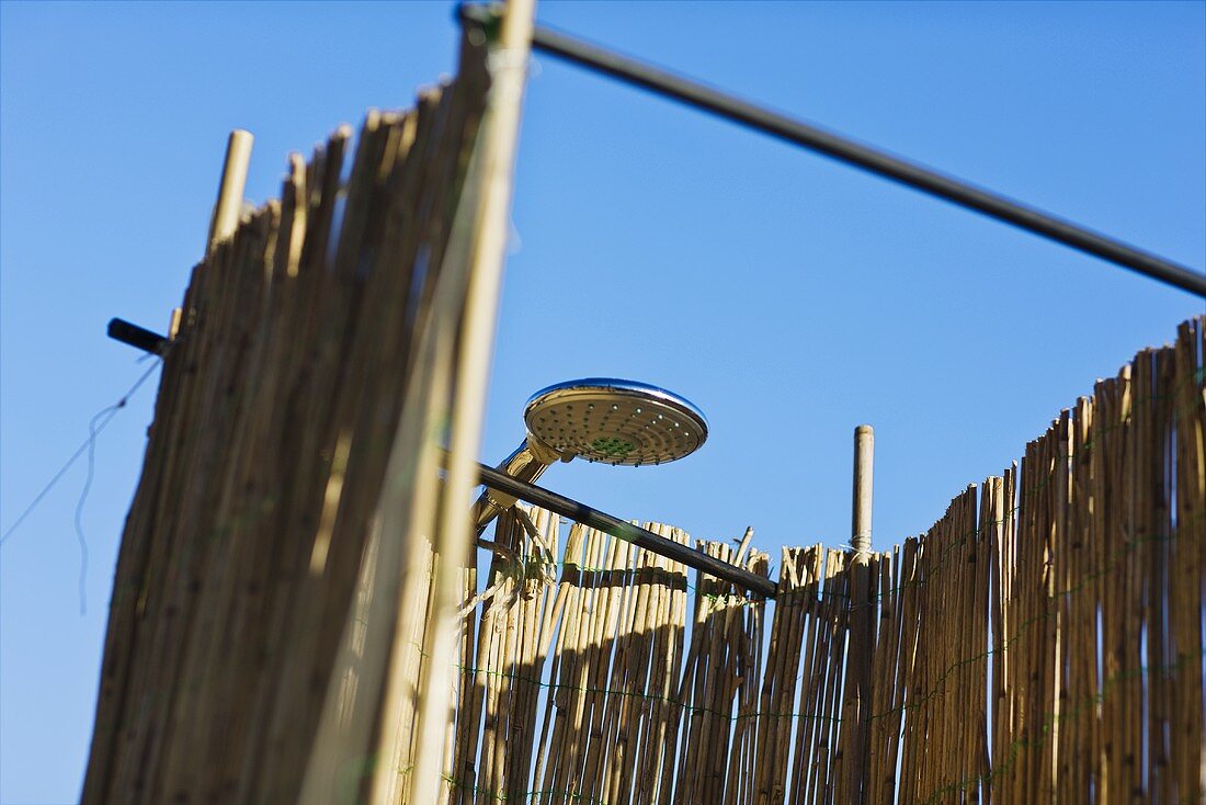 A showerhead in an outdoor shower cubicle with bamboo walls