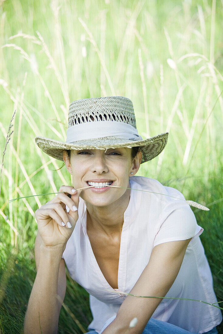 Woman in field, blade of grass between lips, looking at camera