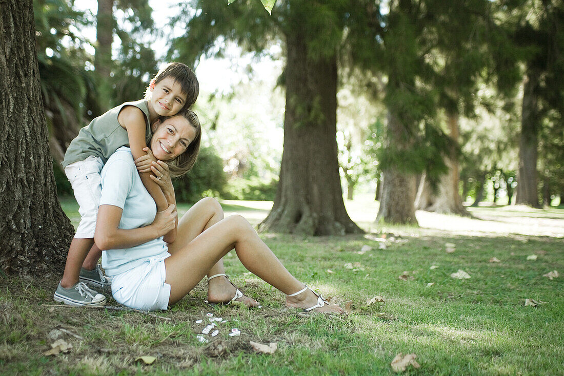 Mother and son sitting outdoors, boy hugging woman from behind