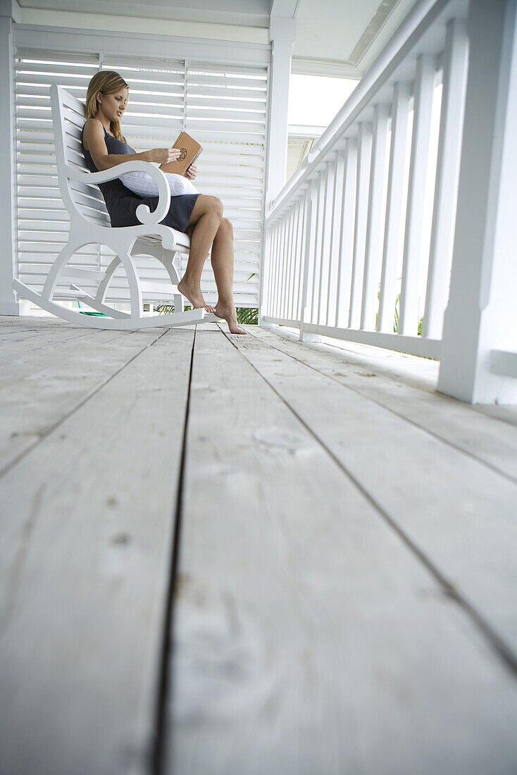 Woman sitting in rocking chair on porch, reading book, low angle view