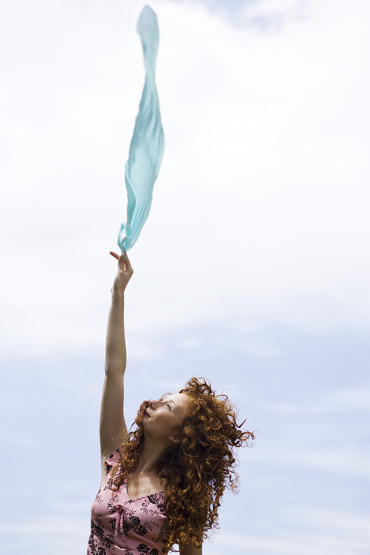 Young woman holding up scarf in wind