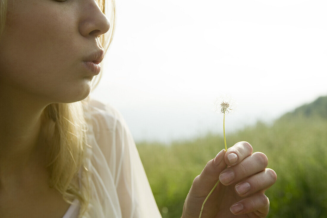 Young woman blowing dandelion seedhead