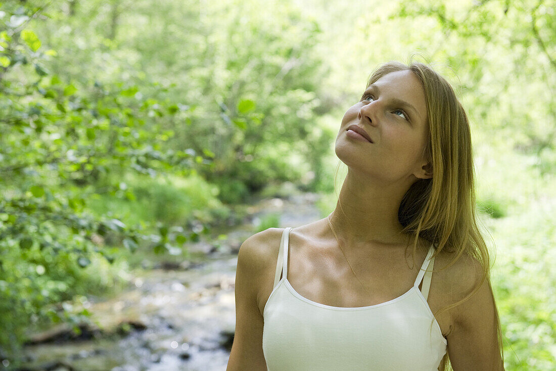 Young woman relaxing outdoors, looking up in thought