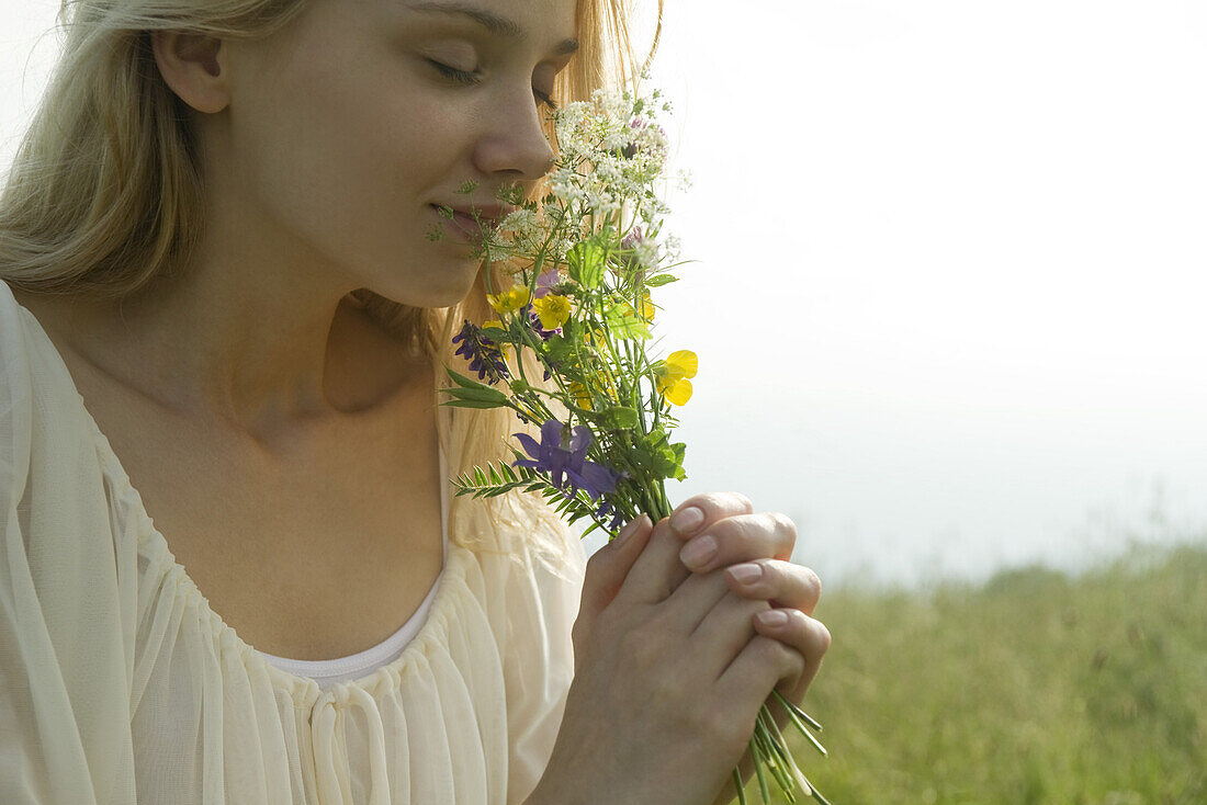 Young woman smelling bouquet of wildflowers, cropped
