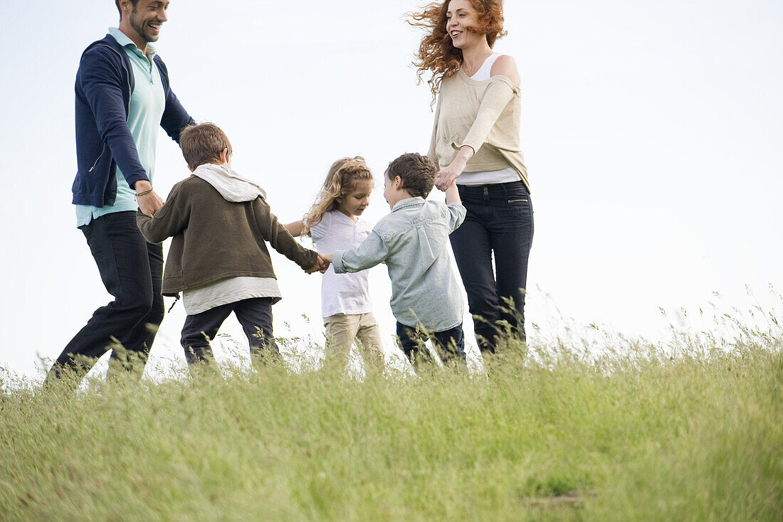 Family playing ring-around-the-rosy in meadow