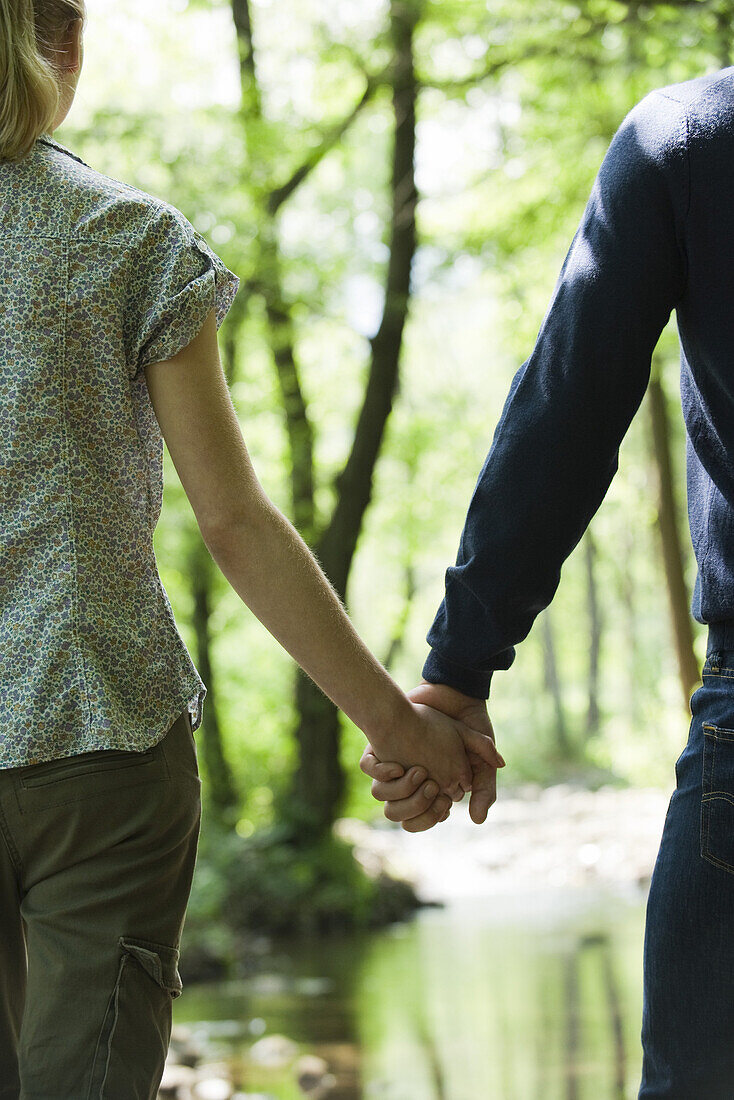 Couple holding hands in woods, cropped