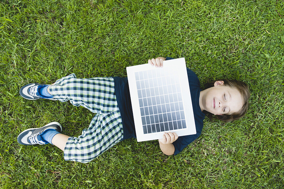 Boy lying on grass holding solar panel