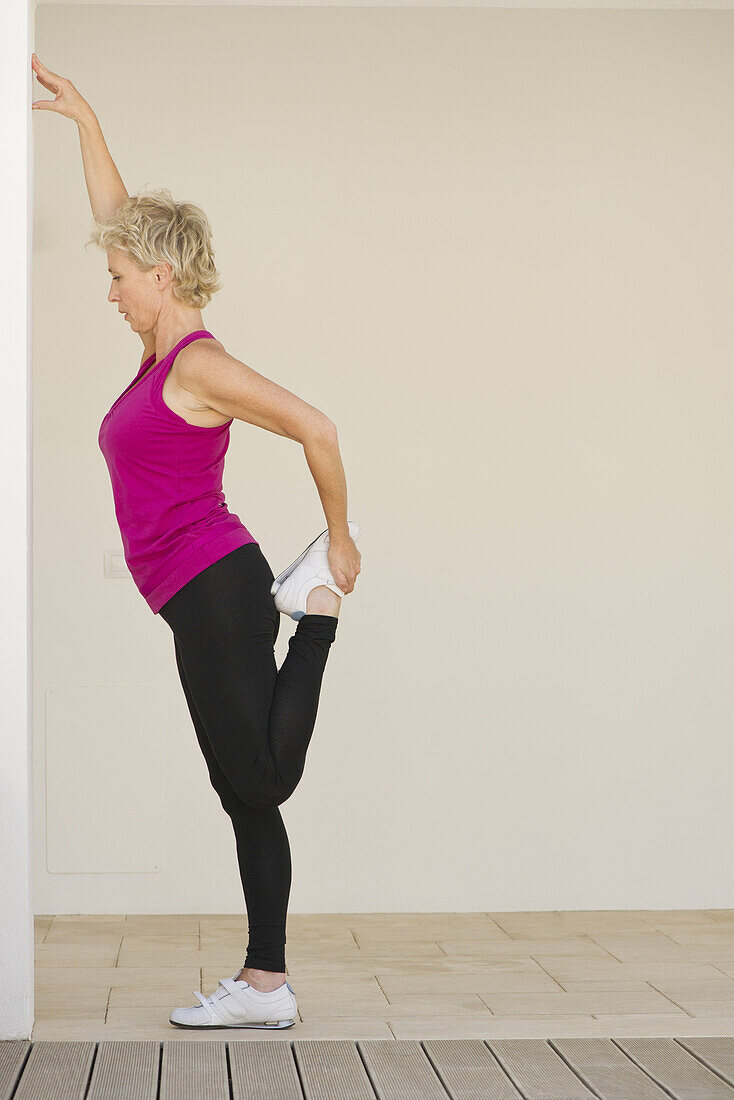 Mature woman stretching against wall, side view
