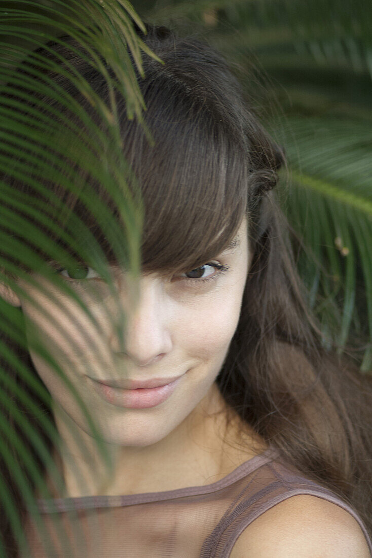 Young woman behind palm frond, portrait